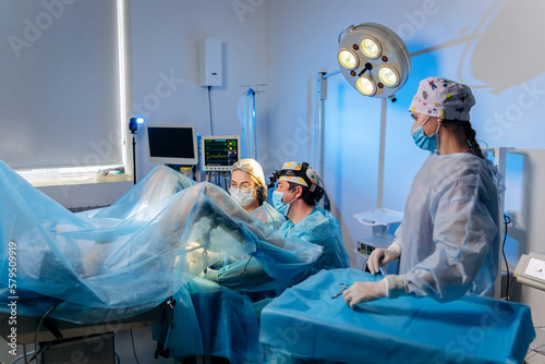Professional team of surgeons proctologist performing operation using special medical devices in the operating room in hospital. Urgent surgical concept
