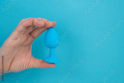 Woman holding a blue anal plug on a blue background. 