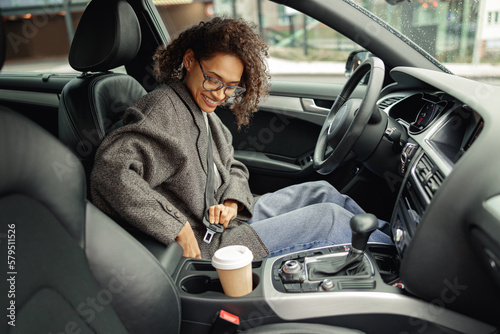 Smiling woman driver in eyeglasses fastens her seat belt before starting car. Driving safety concept photo
