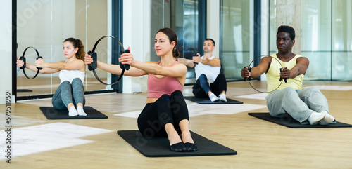 Young sporty men and women doing exercises with pilates circle at group class
