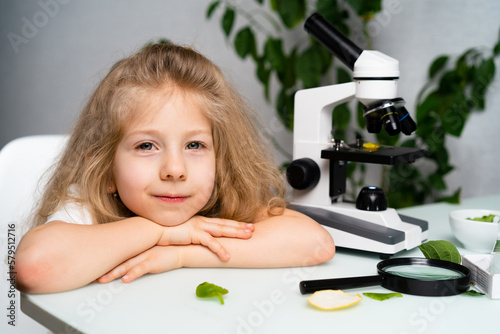 a little blonde girl at a table studying plants with a magnifying glass and a microscope, the concept of ecology and biology, earth day photo