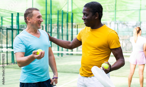Two men with rackets in their hands chatting after playing padel on the tennis court