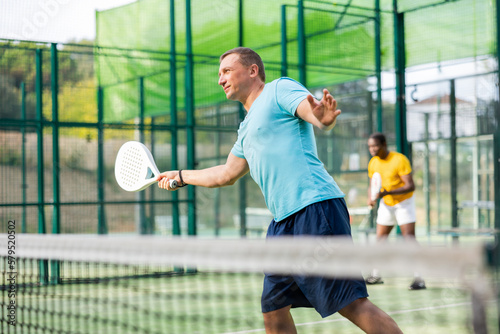 Man in t-shirt playing padel tennis on court. Racket sport training outdoors. © JackF