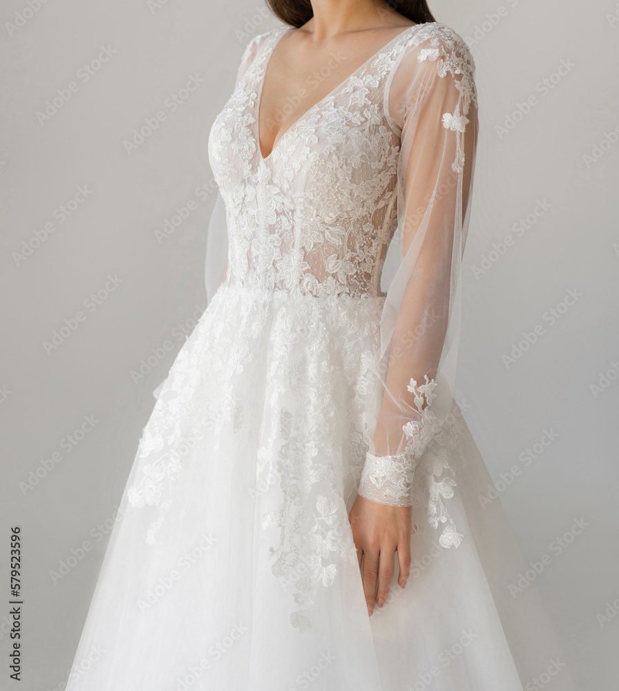 Bride dressed in a white wedding dress with a deep neckline, laced corset and fancy long sleeves. Gorgeous long white wedding dress with transparent sleeves and floral lace.