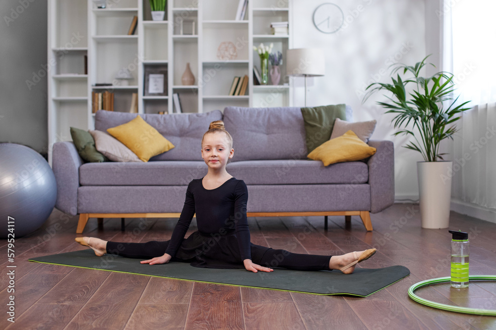 Little girl practicing stretching in room. Physical exercises for children at home. Concept of sport Little girl practicing stretching in room. Physical exercises for children at home. Concept of sport