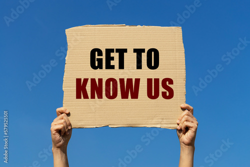 Get to know us text on box paper held by 2 hands with isolated blue sky background. This message board can be used as business concept to inform audience to know us more.