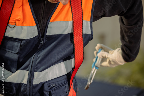 Cropped electrician with orange vest, taking a tool from his worker belt. Horizontal