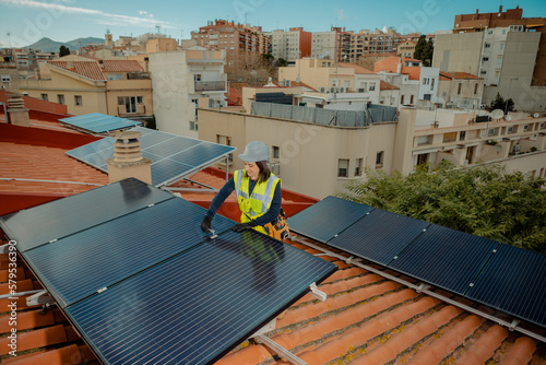 Female electrician engineer installing solar energy panels on city residential rooftop. Woman doing the maintenance of photovoltaic cells for Alternative renewable energy. Wide view, Horizontal