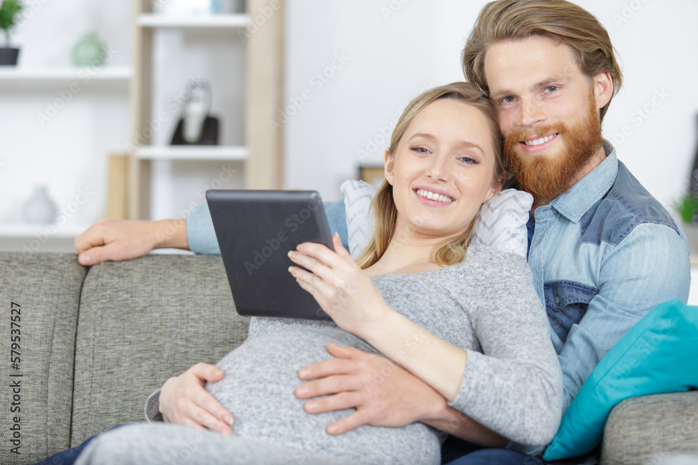 beautiful young pregnant couple with tablet computer sitting on sofa beautiful young pregnant couple with tablet computer sitting on sofa