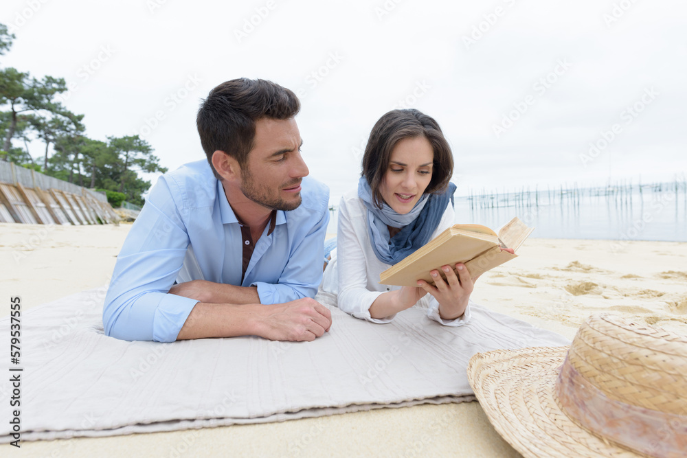 couple lay on the beach reading a book