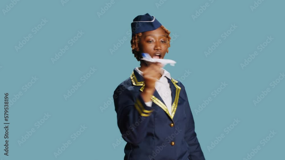 Professional airliner showing fake miniature plane, playing with artificial mini airplane toy on camera. Confident stewaress having fun with small imitation flying aircraft on blue backdrop. Professional airliner showing fake miniature plane, playing with artificial mini airplane toy on camera. Confident stewaress having fun with small imitation flying aircraft on blue backdrop.