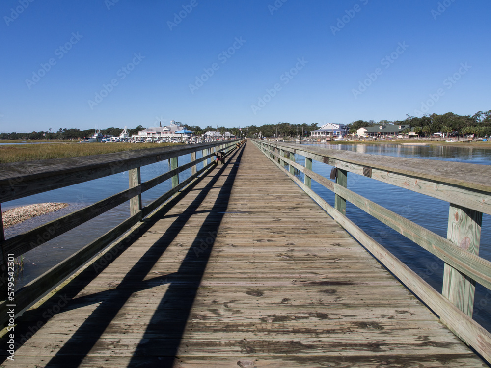 The long wooden pier looking inwards at at Murrell's Inlet, south of Myrtle Beach, South Carolina, USA, on a sunny day with blue sky.