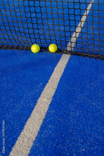 Two ball next to the net of a blue paddle tennis court. © Vic