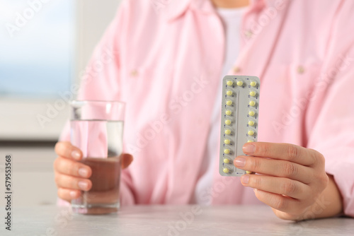 Woman taking oral contraception pill at light grey table indoors, focus on hand