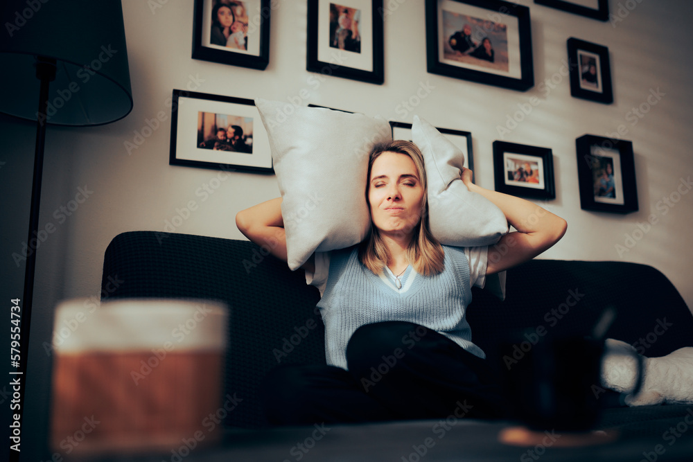Woman Sitting on a Sofa Covering her Ears with Pillows. Unhappy lady