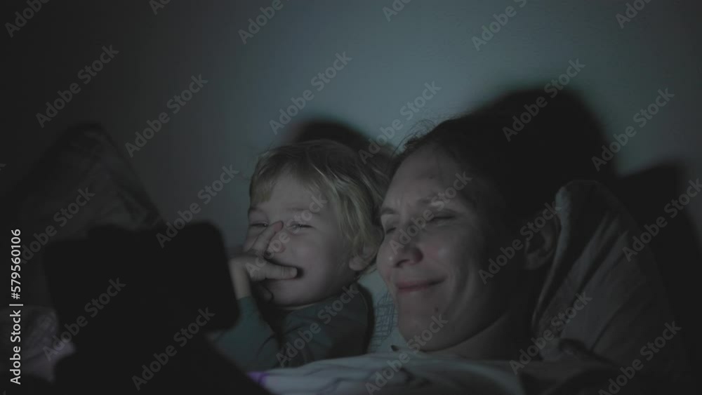 Mom and son lie in bed with the lights off and stare at the phone