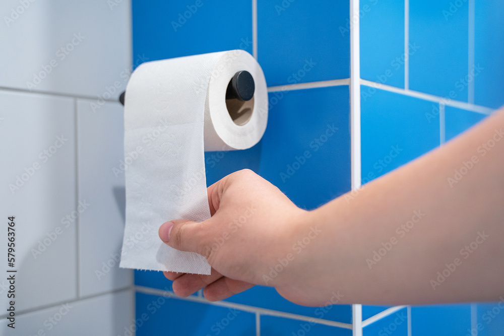 Hand pulls toilet paper hanging from a holder on the wall. Public