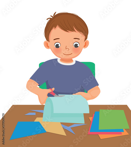 Cute little boy cutting colored paper with scissors making paper cut art craft
