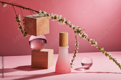 Front view of glass bottle without label, wooden geometries, transparent balls, flower branch and their shadow on pink background. Scene mockup for cosmetic product, copy space. photo