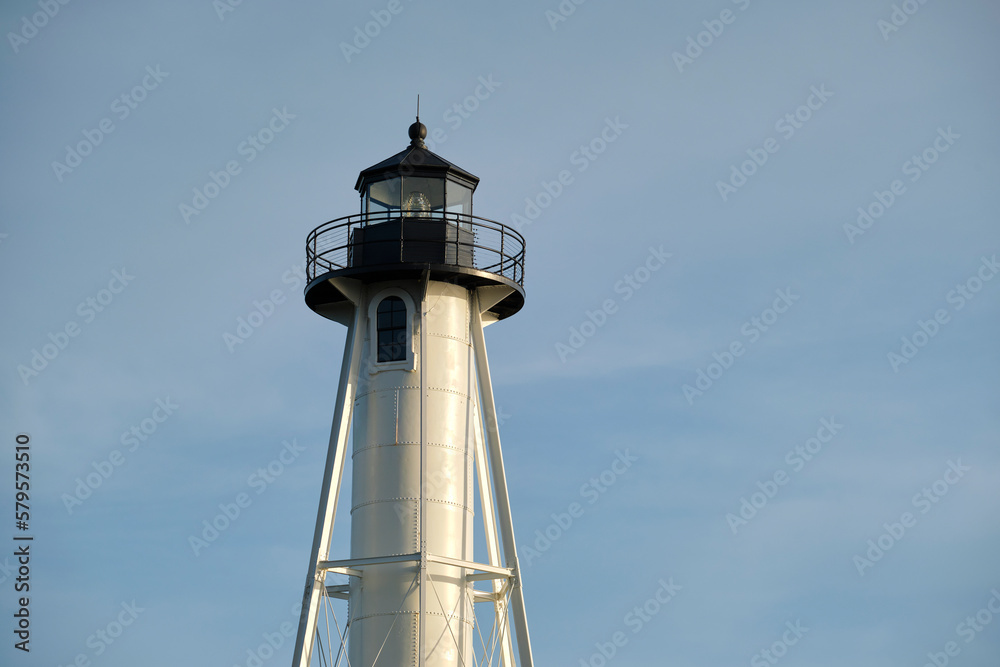 White tall lighthouse on sea shore against blue sky for commercial vessels navigation
