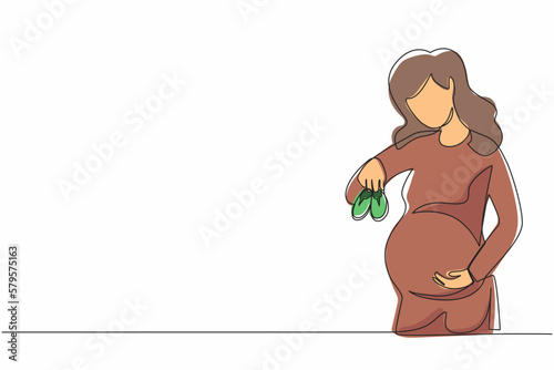 Single continuous line drawing small shoes for unborn baby in belly of pregnant woman. Pregnant woman holding small baby shoes relaxing at home in bedroom. Dynamic one line draw graphic design vector
