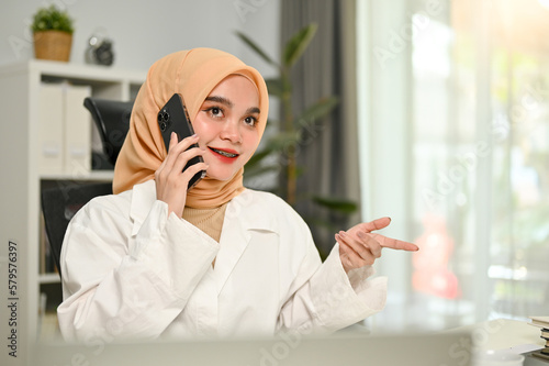 Professional Asian Muslim businesswoman talking on the phone with her business partner