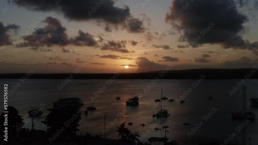 Dolly in aerial shot of the alligator beach, a river in Cabedelo, Paraiba, Brazil, near the coastal capital city of Joao Pessoa, with tour boats watching the sunset as a man plays the saxophone below Dolly in aerial shot of the alligator beach, a river in Cabedelo, Paraiba, Brazil, near the coastal capital city of Joao Pessoa, with tour boats watching the sunset as a man plays the saxophone below