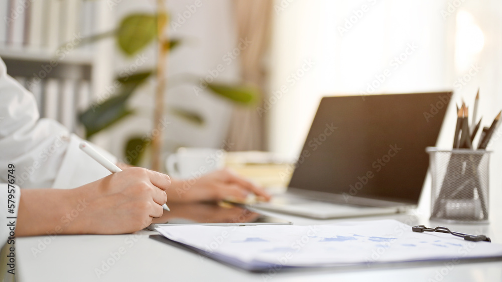 Cropped side view image of a businesswoman working at her desk, using laptop and tablet Cropped side view image of a businesswoman working at her desk, using laptop and tablet