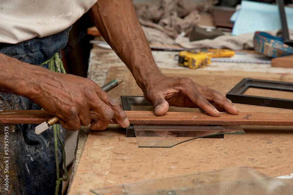 Carpenter cuts glass with his glass cutter to make a window. Man uses cutting tools, Close-up of carpenter's hands cutting glass to size