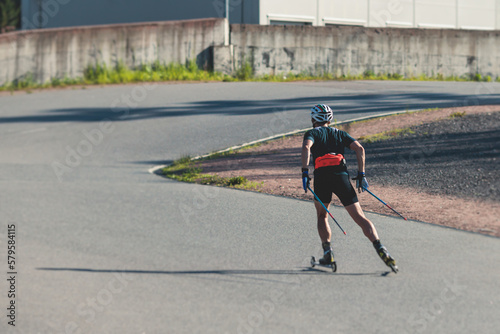 Athletes ride roller skis on asphalt track, group of ski rollers in helmet, cross-country skiing with roller ski in summer sunny day, sportsmen ski-rollers riding, biathlete training  photo