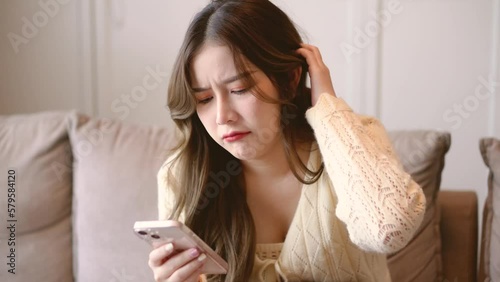 stressful asian women sit on sofa in livingroom looking smartphone and disappointed