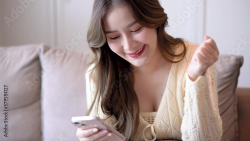 smile asian women sit on sofa in livingroom looking smartphone and celebrate