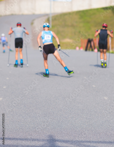 Athletes ride roller skis on asphalt track, group of ski rollers in helmet, cross-country skiing with roller ski in summer sunny day, sportsmen ski-rollers riding, biathlete training 