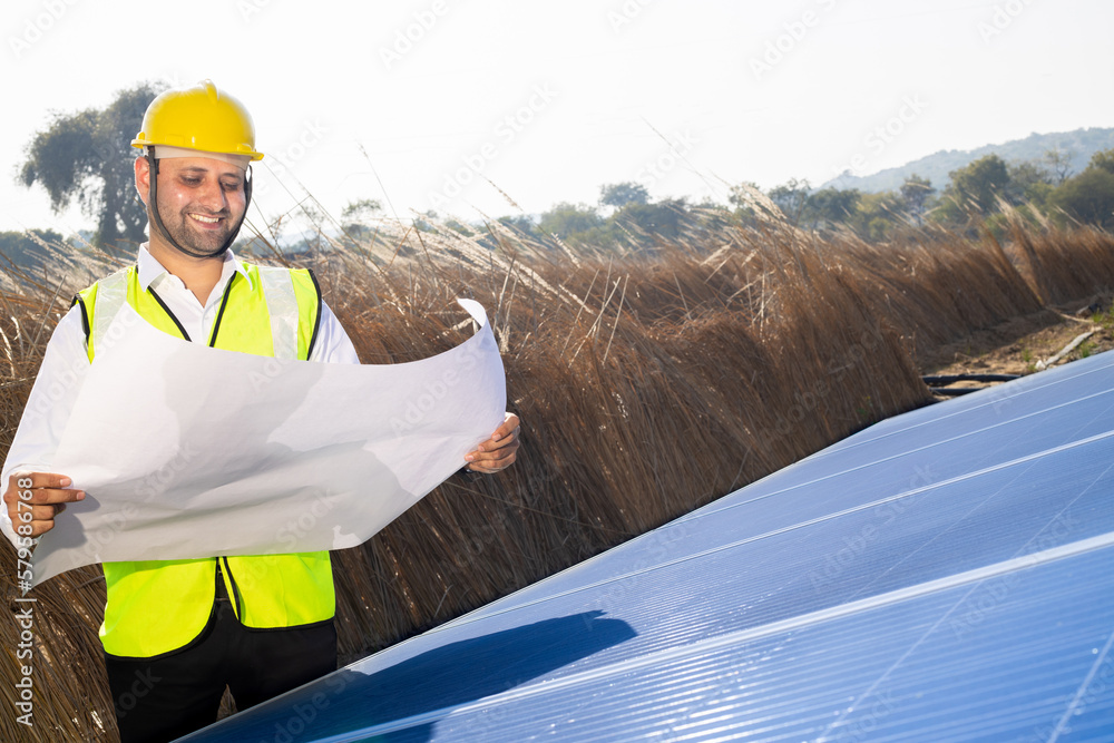 Young indian man technician wearing yellow hard hat standing with chart