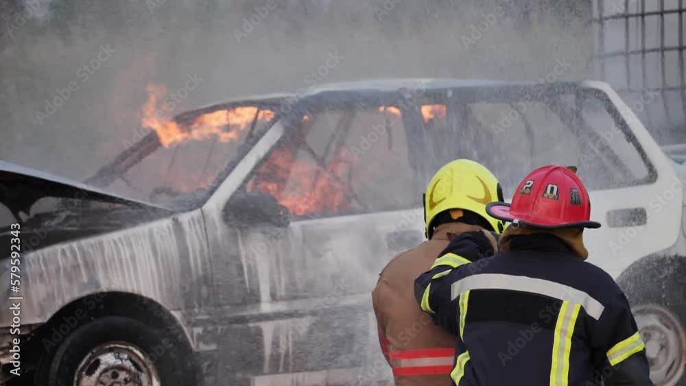 Rear view of Asian fireman wear fire protection suit. Firefighter fighting with fire on a car during fire drill Traffic Accident at Fire station Concept. Slow motion