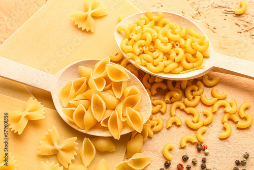 Wooden spoons of raw pasta on color background, closeup