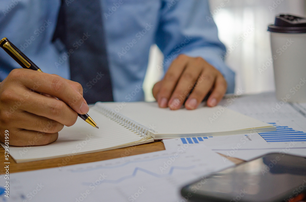 Businessman using pen writing note book planning journal and analysis information statistics document on desk. Businessman using pen writing note book planning journal and analysis information statistics document on desk.