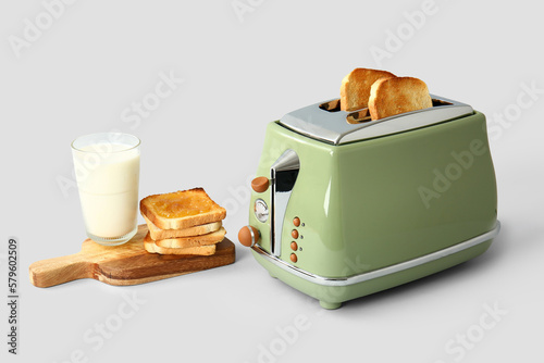 Bread slices in modern toaster, glass of milk and tasty toasts with jam on white background