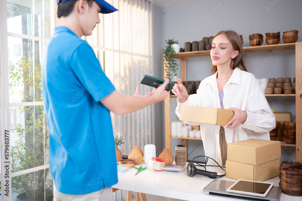 Obraz premium Young woman signs her name on a smartphone after receiving a box of items from the delivery person.