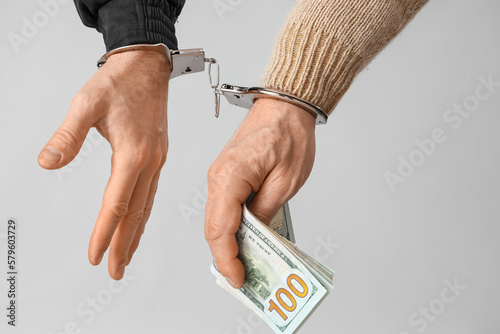 Handcuffed police officer and man with bribe on grey background, closeup