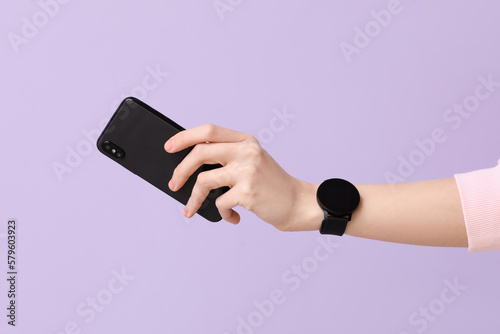 Woman with smartwatch and mobile phone on lilac background photo