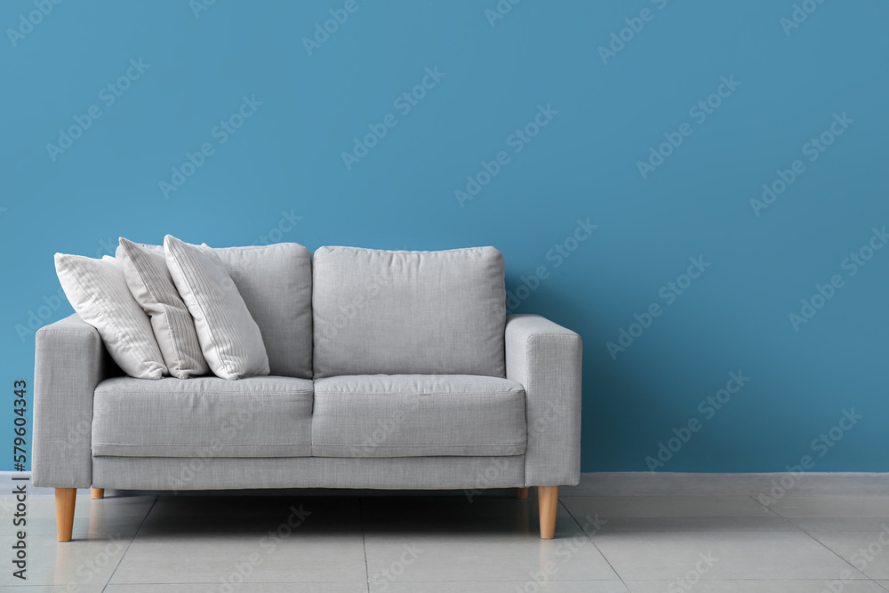 Fototapeta premium Stylish decorative pillows on cozy grey sofa near blue wall