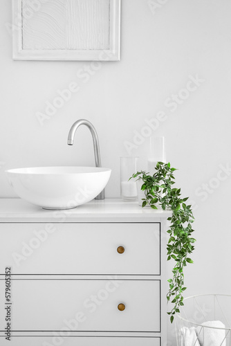 Sink with candles and houseplant on chest of drawers in bathroom
