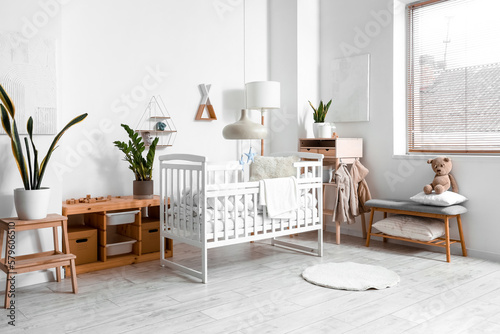 Interior of light children s bedroom with baby crib  table and bench