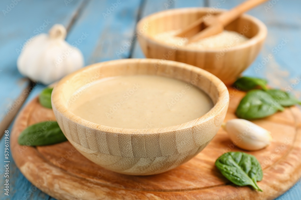 Board with bowl of tasty tahini, sesame seeds, spinach and garlic on color wooden table, closeup Board with bowl of tasty tahini, sesame seeds, spinach and garlic on color wooden table, closeup