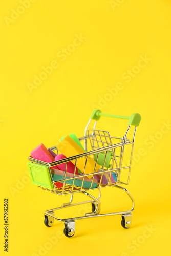 Shopping cart with erasers and chalk on yellow background