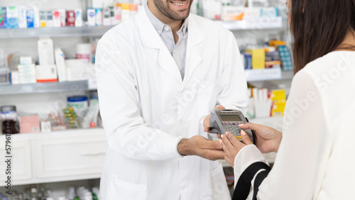 Customer making payment using credit card with swipe through terminal. Woman entering pin code in swipe machine in modern pharmacy.