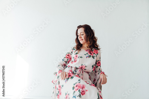 a woman in a floral dress sits against a white wall on a white background