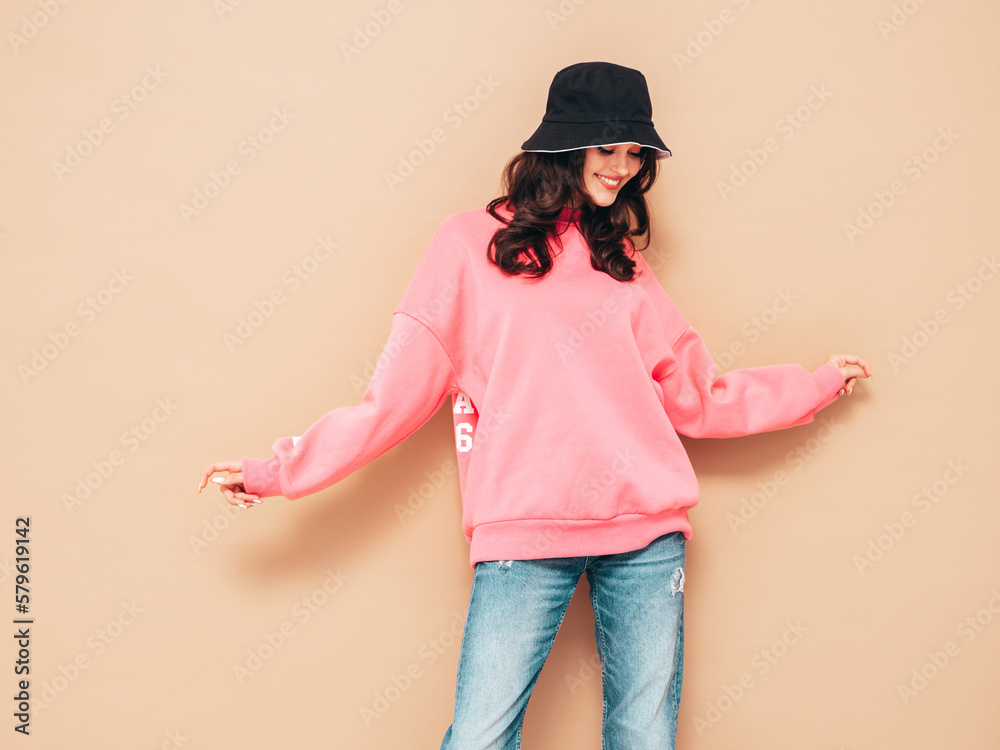 Young beautiful smiling female in trendy summer jeans and pink sweater clothes. Sexy carefree woman posing near beige wall in studio. Positive model. Cheerful and happy. In panama Young beautiful smiling female in trendy summer jeans and pink sweater clothes. Sexy carefree woman posing near beige wall in studio. Positive model. Cheerful and happy. In panama