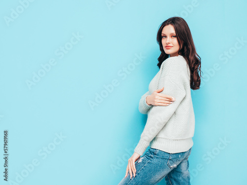 Young beautiful smiling female in trendy summer jeans and warm winter sweater clothes. Sexy carefree woman posing near blue wall in studio. Positive model. Cheerful and happy. Isolated.